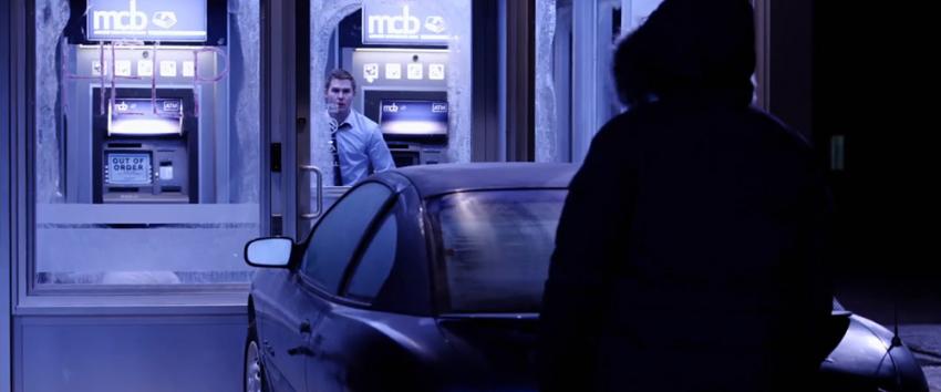 ATM (1970) Movie scene: An intense standoff between David (Brian Geraghty) and the antagonist, with a crashed car positioned between them, slammed against the ATM booth