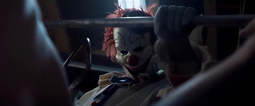 Clown in a Cornfield (1970) Movie scene: Frendo the Clown holds a saw in one hand and grips a barbell with the other, staring down at his victim.