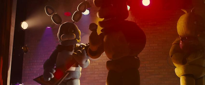 Five Nights at Freddy's (1970) Movie scene: Animatronic characters stand on stage under colorful lights, including a rabbit with a guitar and a bear with a microphone