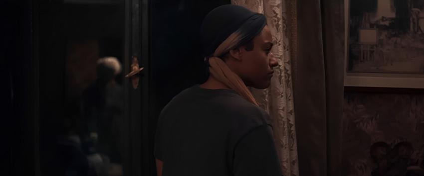 House of Spoils (1970) Movie scene: Chef (Ariana DeBose) stands with her back turned, as the reflection of an elderly woman appears in the window behind her