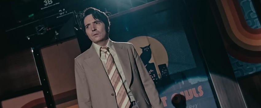Late Night with The Devil (1970) Movie scene: Jack Delroy (David Dastmalchian) stands in front of the Night Owl show logo, looking harrowed
