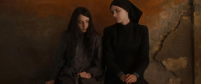 The First Omen (1970) Movie scene: Carlita (Nicole Sorace) and Margaret (Nell Tiger Free) sitting together against a cracked facade.