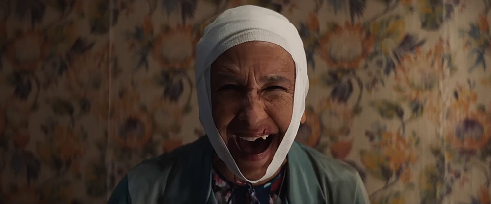 The Front Room (1970) Movie scene: Solange (Kathryn Hunter) in a close-up front-facing shot, grinning with her head wrapped in a bandage